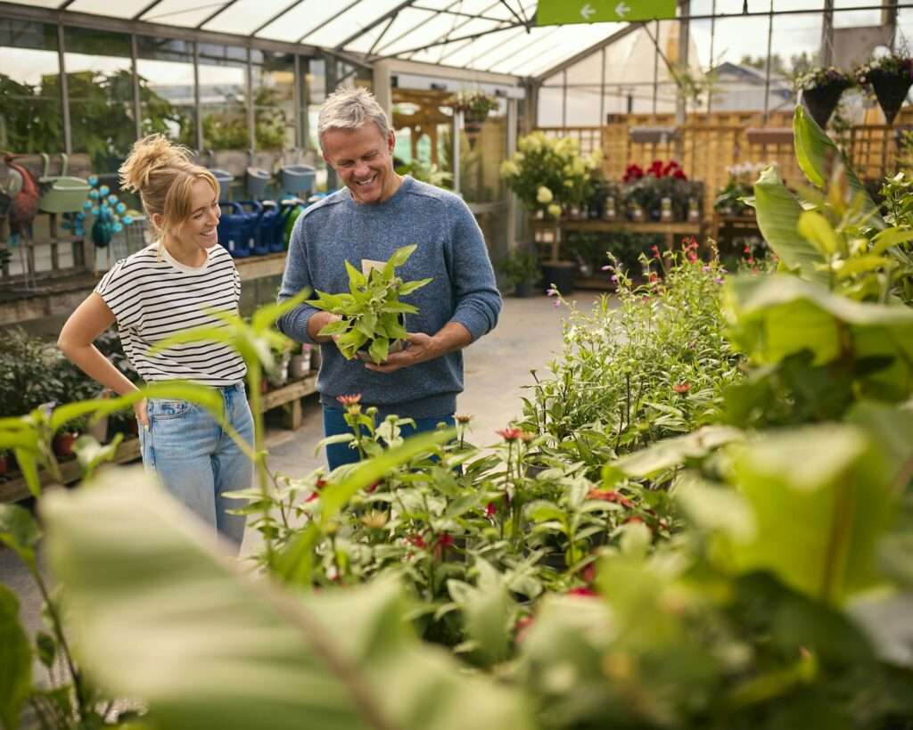 Couple Inside Greenhouse In Garden Centre Choosing And Buying Plants