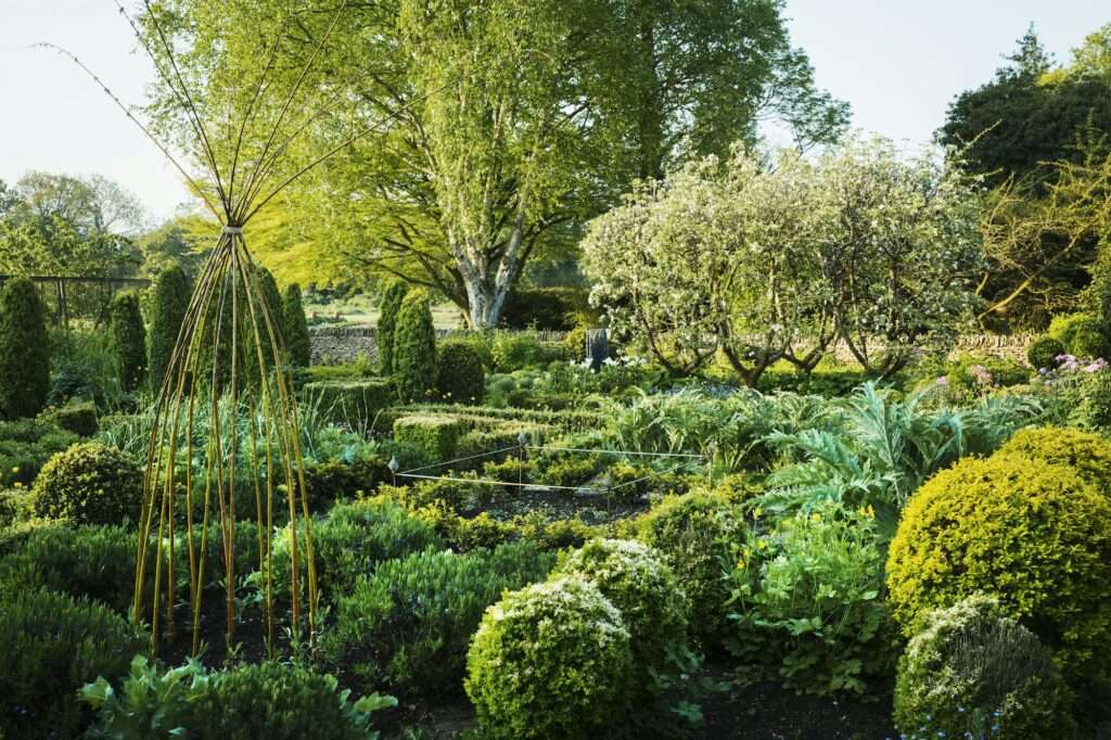 View of garden with flower beds, shrubs and trees in the background.