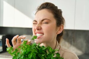 Funny and cute brunette woman bites delicious, fresh green parsley, eating herbs, cooking salad in