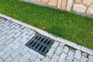 Plastic drain gutter, green grass lawn and stone pavement sidewalk.