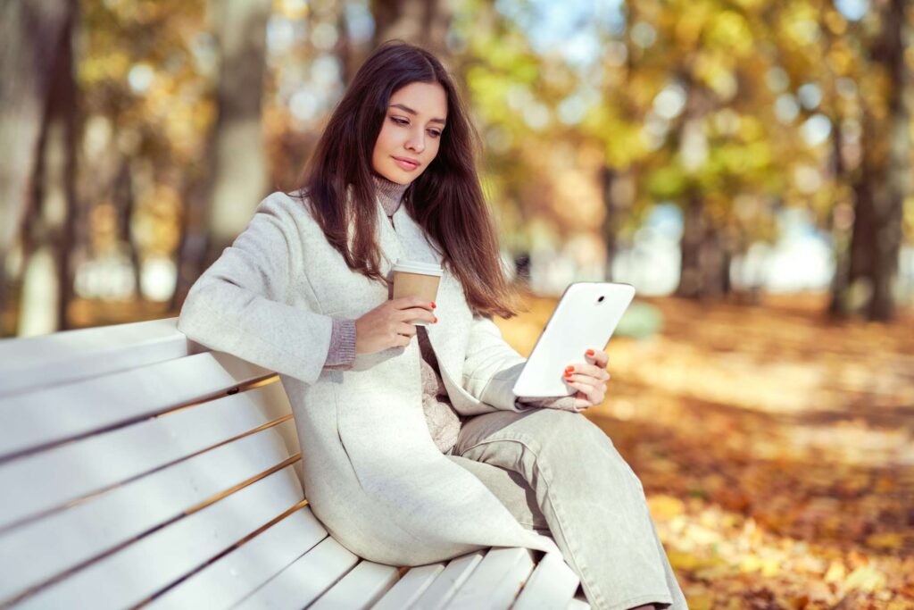 Young beauty woman sitting with a cup of coffee on a bench in the fall park