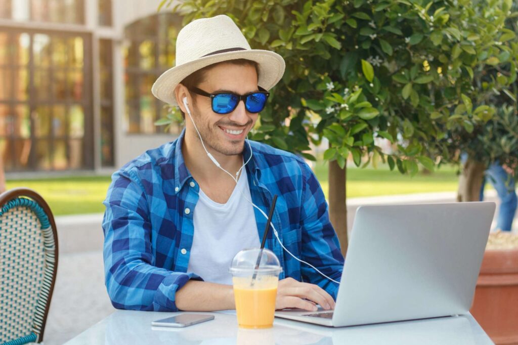 Young smiling European blogger sitting at cafe table enjoying summer time outside