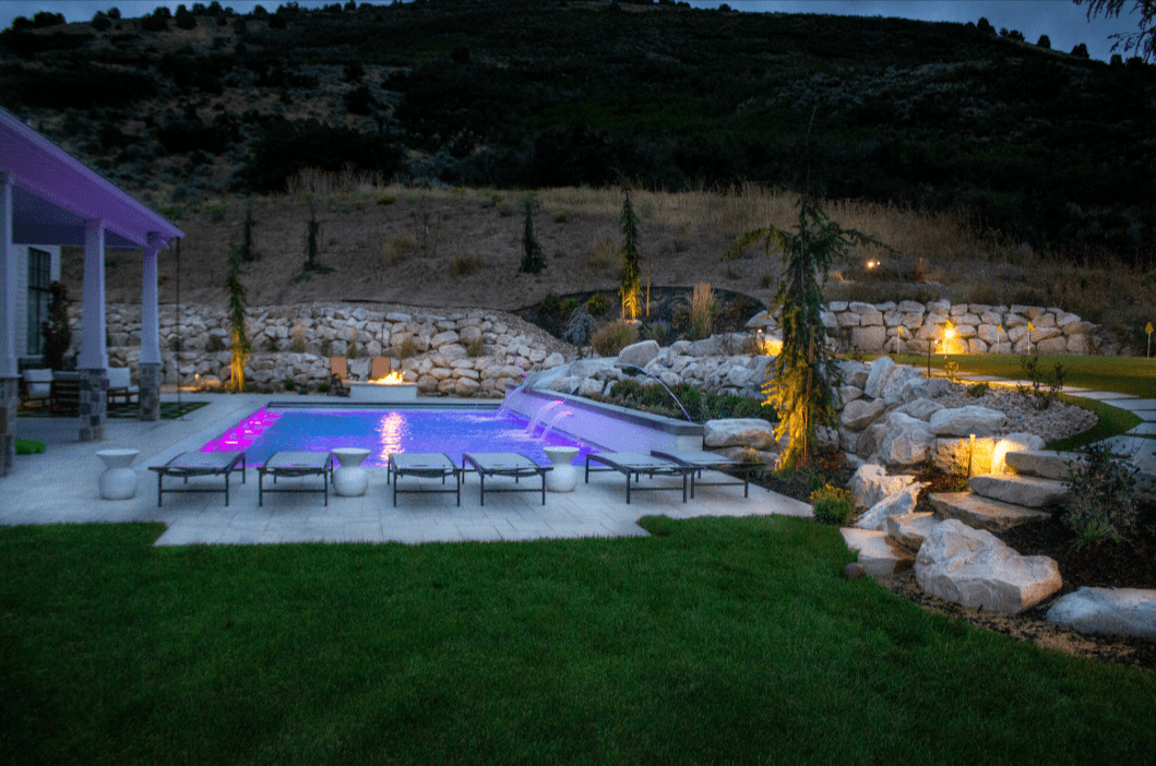 Luxury landscape design featuring a pool with purple lighting and stone accents.