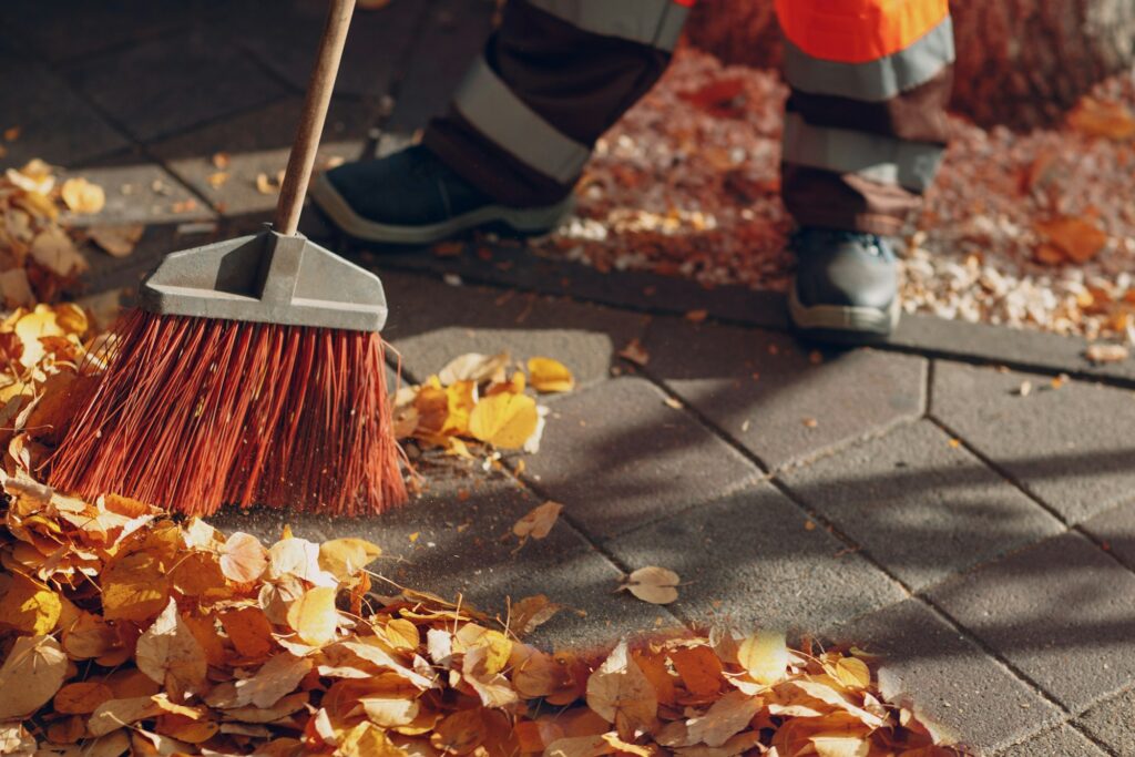 Worker sweeping away fallen autumn leaves with broomstick