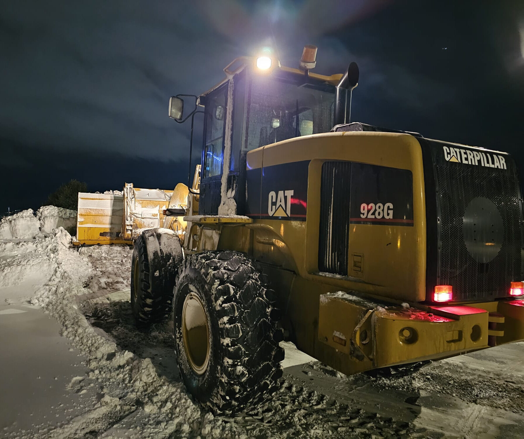 Caterpillar 928G wheel loader removing snow at night on a city construction site