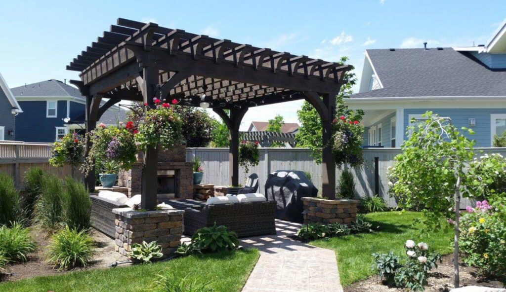 Modern backyard pergola with outdoor seating, stone fireplace, hanging flower baskets, and landscaped garden in a residential home
