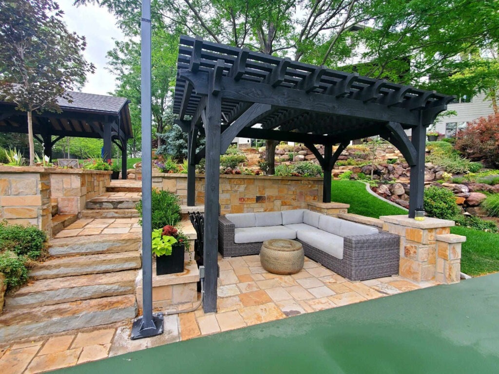 A South Jordan Utah backyard patio showing the perfect balance of beautiful stone pavers, a louvered pergola, outdoor kitchen, and lush drought-tolerant landscaping